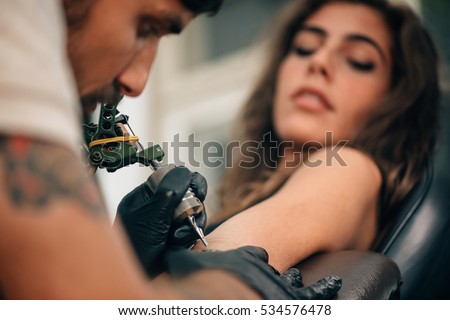 Tattoo artist creating a tattoo on a girl\'s arm. Focus on tattoo machine