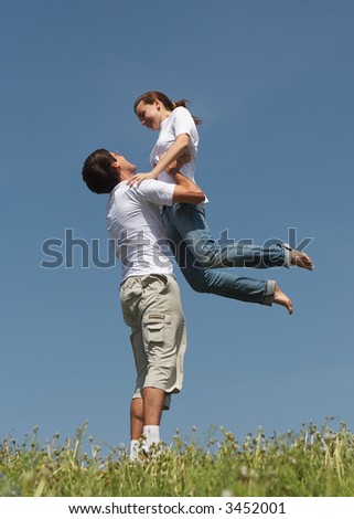 Man holds the girl on hands standing on a green grass on a background of the blue sky