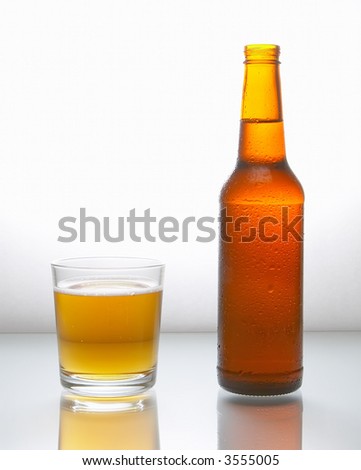 Bottle with beer and a glass filled with beer with foam on a white reflecting surface