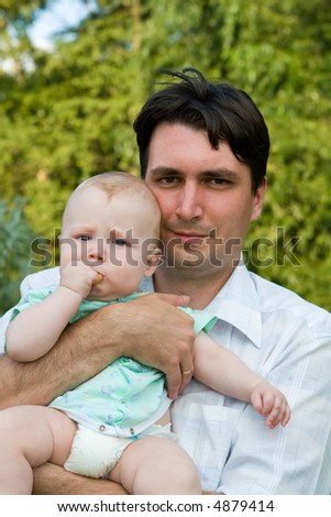 Father holds on hands of the small child on a background of green foliage