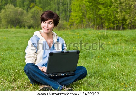 Young attractive girl sits on a green grass with a portable computer