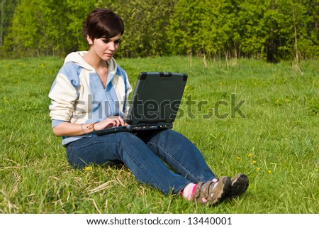 Young attractive girl sits on a green grass with a portable computer