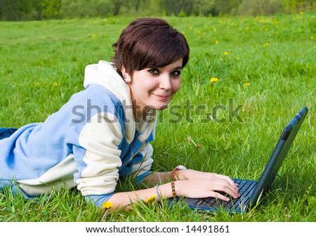 Girl sits on a green grass with a portable computer