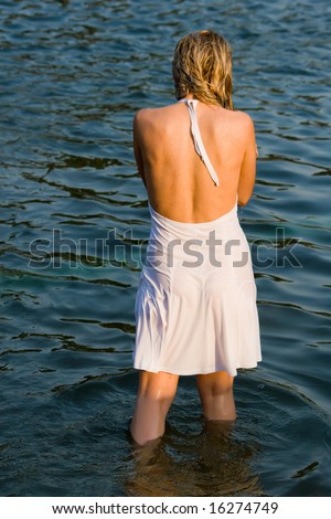 Girl in a white dress stands in water having turned a back