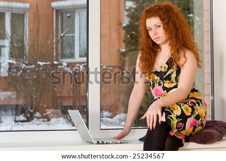 Beautiful young woman sits near a window with mobile computer