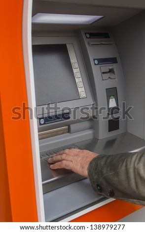 Man at ATM or cash dispenser and  entering PIN; only hand to be seen