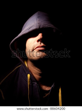 Portrait of a man with a cowl covering his eyes. Studio lighting. Half face illuminated, half face in shadows.