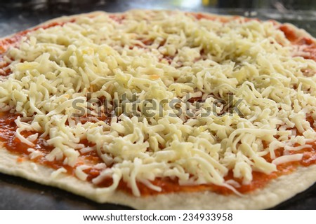 Cheese covering pizza preparation on wooden board.