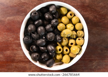 green and black olives in white bowl on wooden background