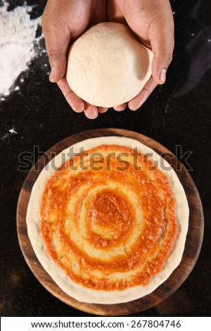 balls of fresh pizza dough in hand and tomato sauce on pizza base