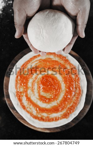 balls of fresh pizza dough in hand and tomato sauce on pizza base,selective color technique