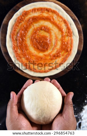 balls of fresh pizza dough in hand and tomato sauce on pizza base