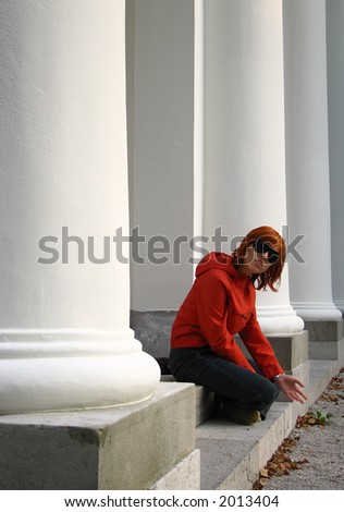 A young redhead sitting in a colonnade and playing with the sand.