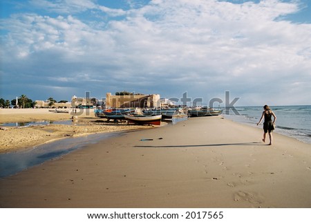 A young woman walking past fishing boats in the late evening light (Tunisia).