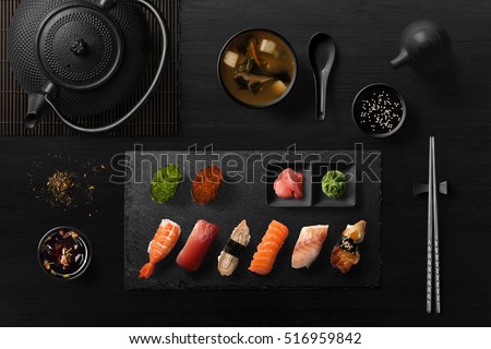 Sushi rolls, sashimi set, miso soup and teapot, on dark wooden table, Japanese food, top view.