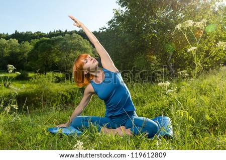 Beautiful red haired woman practicing fitness yoga outdoors on a summer day