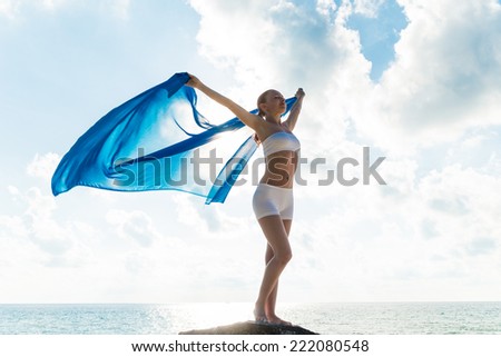 Freedom and beauty concept. Beautiful girl with blue scarf standing on the Rock. Flying. Free. Vacation
