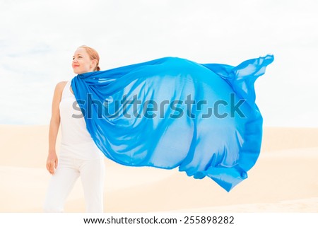 Young slim woman wearing white with flying blue scarf in desert