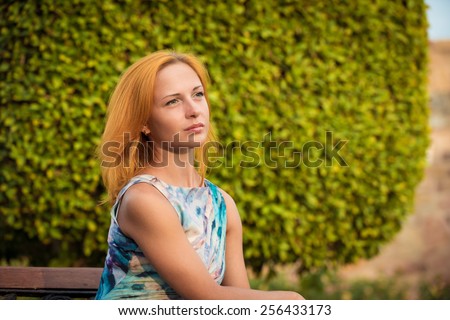 Young red woman wearing long dress sitting on a bench