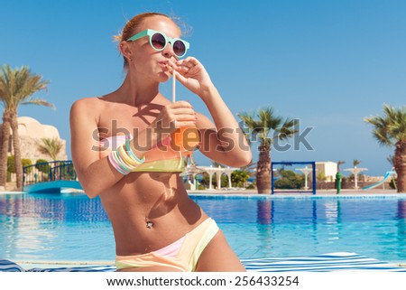 Happy young woman with cocktail on chaise-longue and enjoying sun