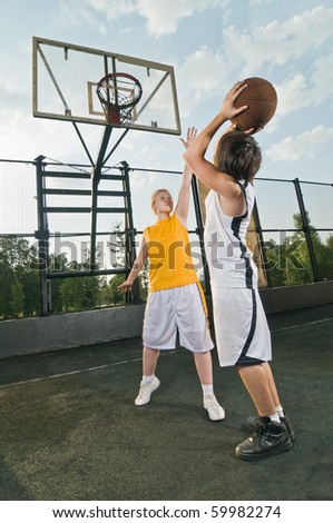 Two teenagers playing basketball at the street playground