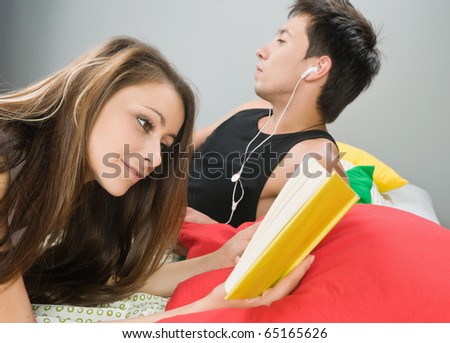 Happy young couple in bed with girl reading a book and boy listening to the music