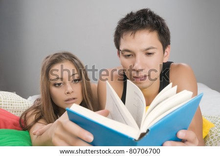 Young couple reading interesting book in bed