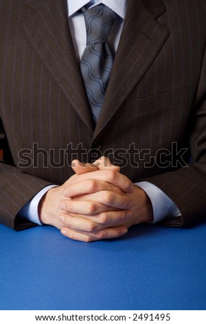 Businessman. Blue table. Hands clasped. Copy space.