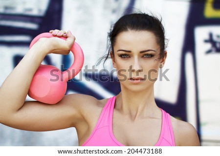 Woman holding pink kettlebell over shoulder, outdoor sport