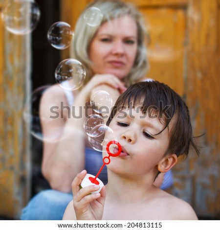Little boy blowing soap bubbles, mother background, motherhood, parenting. Happy family.