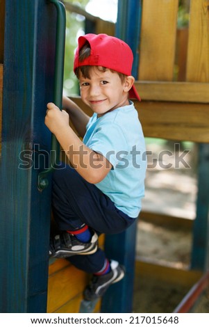 Little boy in cap climb up on jungle gym