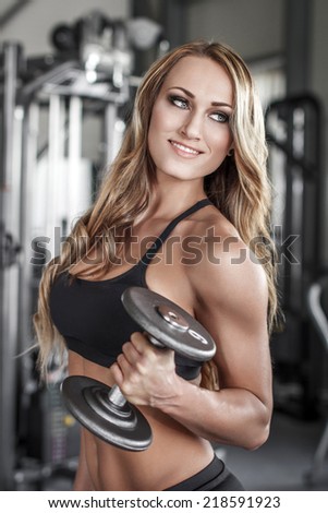 Female fitness model posing with dumbbell in gym