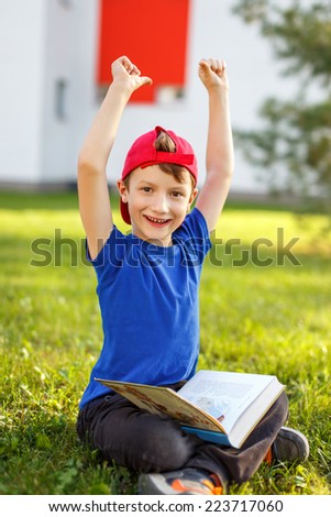 Happy little boy in cap sit with book outdoor, knowledge, education