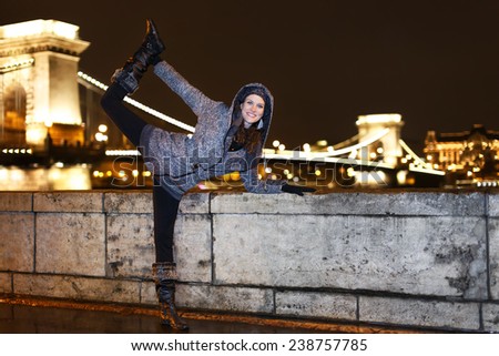 Dynamic woman posing at river Danube at night, Szechenyi chain bridge background, Budapest, Hungary.