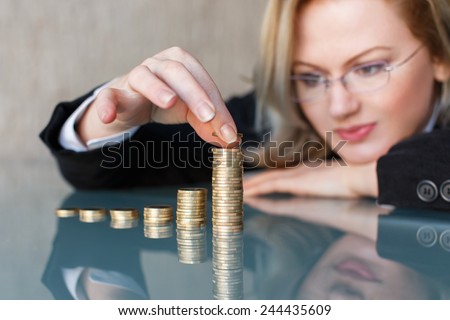 Blonde businesswoman in glasses building growing one euro columns, saving money concept.