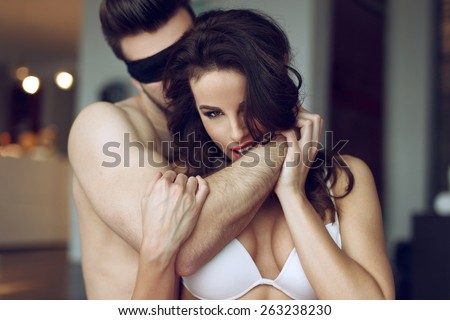 Passionate couple foreplay in luxury flat, sexy woman in bra bite man arm, young lover with lace eye cover