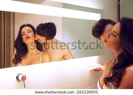 Sexy man kissing woman neck at mirror in bathroom, passionate couple