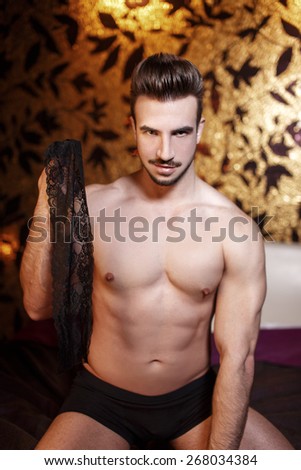 Sexy naked macho man holding lace eye cover in luxury hotel room