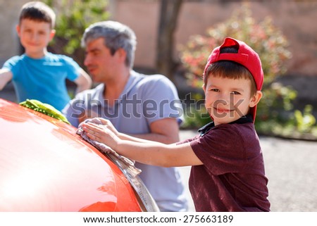 Family car wash day, little boy cleaning spotlight, father and brother in background out of focus