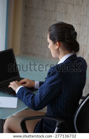Brunette businesswoman typing on laptop in office, back view