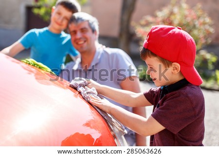 Little boy in cap washing car with dad and brother, fun with family