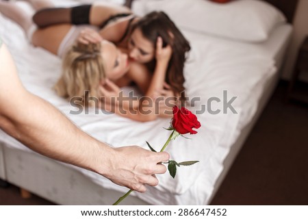 Sexy macho holding rose lesbian lovers in background, threesome