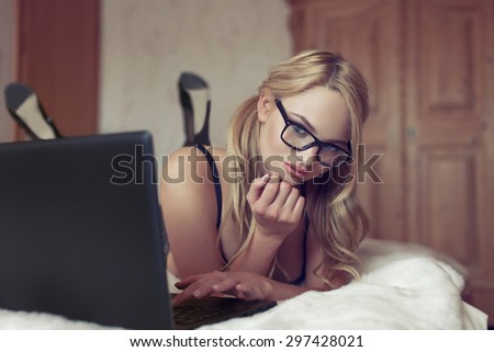 Sexy blonde woman in glasses typing on laptop at home