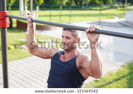 Sporty man pull-up outdoor in park on horizontal bar