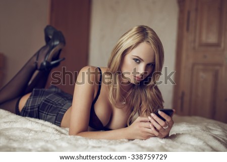 Sexy woman in bra lying on bed write message by phone