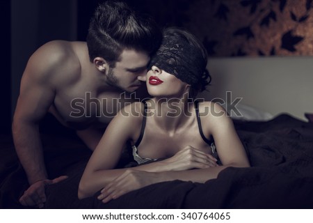 Sexy woman in lace eye cover and red lips with young lover, foreplay in hotel room