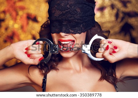 Sexy woman bite handcuffs in lace eye cover, red lips and nails