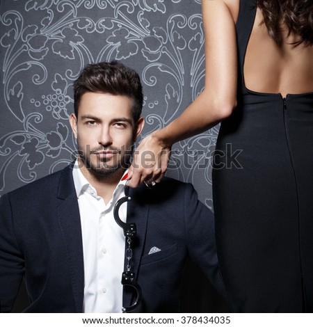 Macho rich businessman with lover holding handcuffs at vintage wall