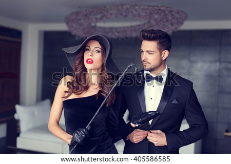 Sexy dominatrix woman posing with whip and young macho lover in tux