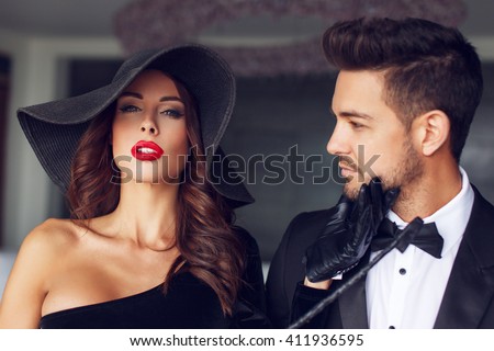 Sexy milf woman in hat with young lover in tuxedo in luxury flat